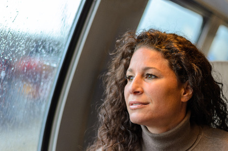 Young woman travelling on a train on a rainy day sitting looking out off the windows at the weather...