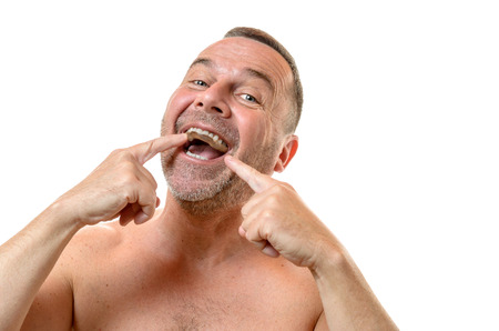 Bare chested man with short hair and stubble points to teeth with two fingers against a white backgroundの写真素材