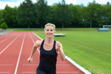 Healthy fit young woman running on a sports track at a stadium as she enjoys her daily workout in a...