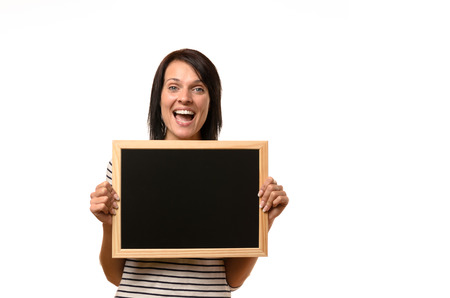 Happy laughing young woman with a blank school slate or chalkboard in her hands with copy space for your text or advertisement isolated on whiteの写真素材