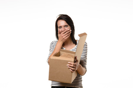 Front view of single surprised woman in striped shirt and brown hair laughing or shocked while holding open cardboard boxの写真素材