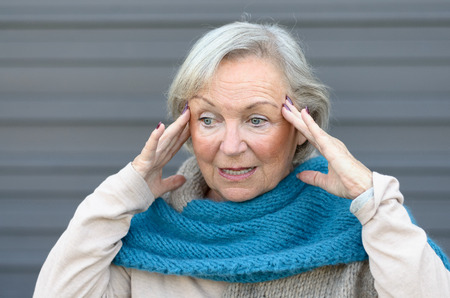 Confused and bewildered senior lady holding her hands to her temples as she looks aside, conceptual of the onset of dementia or Alzheimers diseaseの写真素材