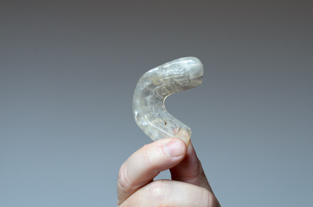Finger holding a bite plate to protect his teeth at night from grinding caused by bruxismの写真素材