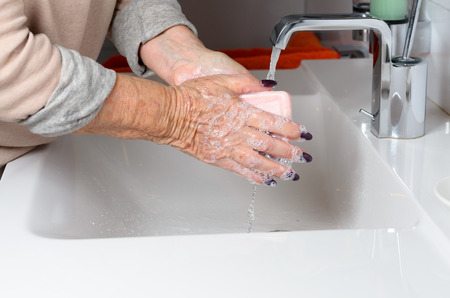 Side view of elderly woman washing hands under running tapの写真素材