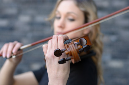 Blurred close-up side portrait of young blonde woman playing violin with focus on the scroll of wooden instrument and left hand of playerの写真素材