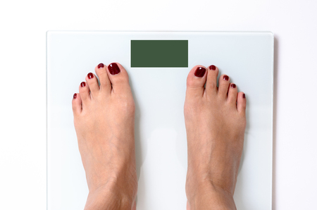 Close-up of woman feet with red nail polish standing on white weight scales with green screen