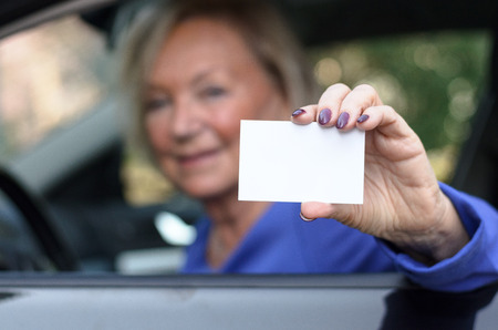 Elderly woman leaning through the open window from the drivers seat of a car showing her licence with a happy friendly smileの写真素材