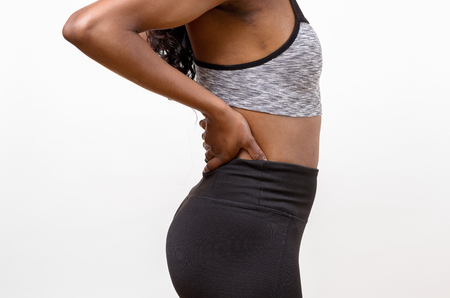Close up athletic woman holding her painful injured back while doing an excerciseの写真素材