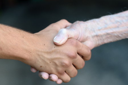 Old and young man shaking or gripping hands in a close up view conceptual of assistance, agreement, acceptance, greeting and toleranceの写真素材