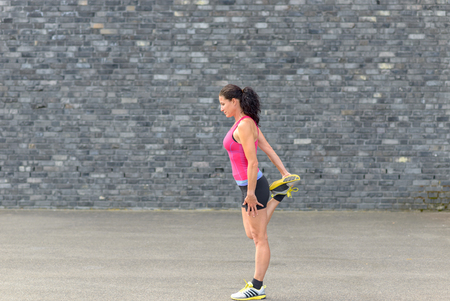Young woman doing warming up exercises to stretch her muscles before working out in side view with...