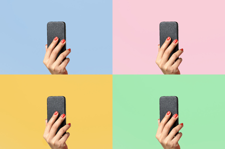 Woman with varnished red fingernails holding up a mobile phone on four different colors of background with copy spaceの写真素材
