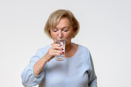 Senior woman drinking a healthy glass of fresh water to quench her thirst in a front view over white with copy spaceの写真素材