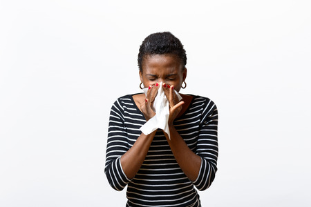 Young African woman blowing her nose on a tissue conceptual of seasonal flu, rhinitis or a respiratory allergy like hayfever isolated on whiteの写真素材
