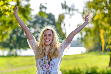 Outdoor portrait of young happy blonde woman raising handsの写真素材