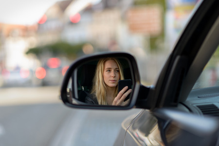 Young blonde girl in car wing mirror while textingの写真素材