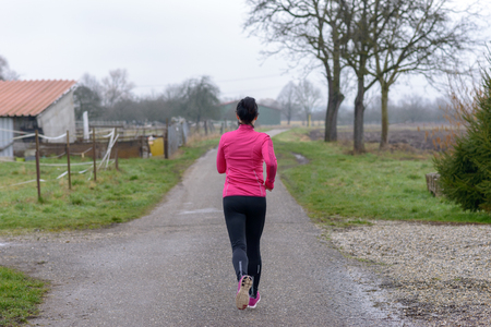 Rear view of a fit young woman jogging along a rural road in winter on a grey day in a healthy lifestyle and fitness conceptの写真素材