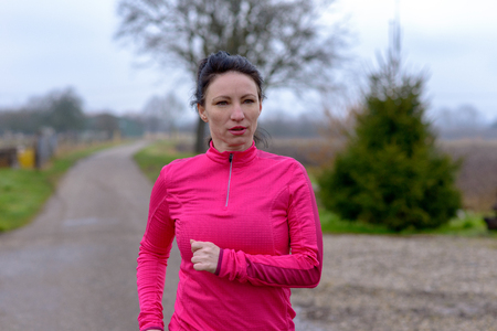 Determined woman jogging along a rural road in winter about to pass the camera in a fitness and healthy active outdoors lifestyle conceptの写真素材