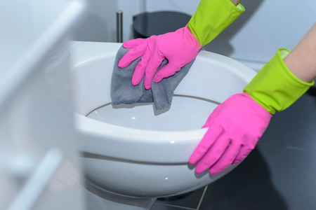 Person wearing colorful bright pink rubber gloves wiping out a toilet bowl with a cloth in a household chores and hygiene conceptの写真素材