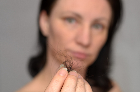 Woman holding a tangle of loose brown hair in her fingers after removing it from the hairbrush with focus to her handの写真素材