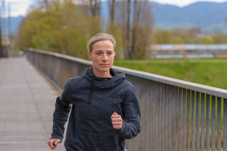 Slender athletic woman jogging on a bridge alongside old rusty metal girdersの写真素材