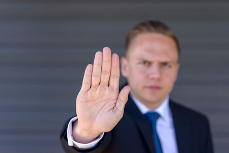 Young businessman giving a halt gesture holding up the palm of his hand with a stern expression and focus to the handの写真素材