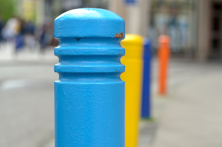 Row of brightly colored safety bollards on a street with focus to a blue one in the foregroundの写真素材