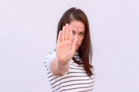 Young brunette woman showing hand stop gesture against neutral background, selective focus