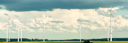 Panorama of a rural wind farm with wind turbines suppling renewable sustainable energy and electricity from the kinetic energy of the wind under a cloudy blue skyの写真素材