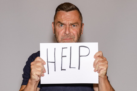 Frightened middle-aged man holding sheet of paper with help lettering against white backgroundの写真素材