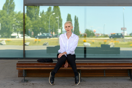 Businesswoman is sitting on a bench in front of a window with reflectionsの写真素材