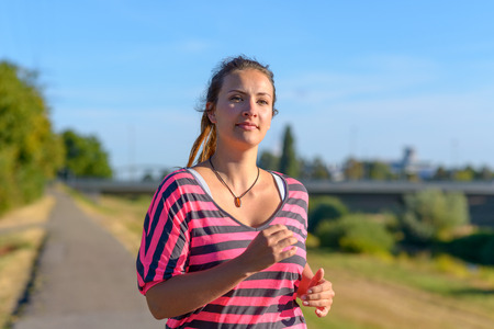 Front view of young smiling woman wearing sportswear running along riverの写真素材