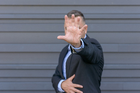Head and shoulders portrait of middle aged man with hand in front of face, focus on hand