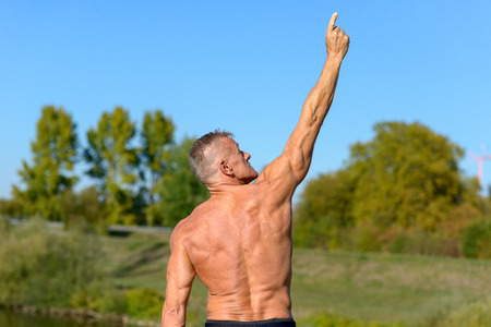 Rear view of a strong man pointing to the sky while standing in a parkの写真素材