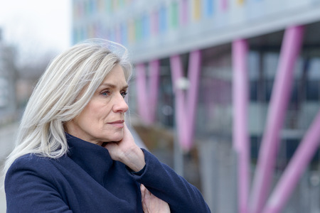 Pensive woman standing staring into the distance as she leans on the railing on an urban walkway resting her chin on her hands in a close up profile portraitの写真素材