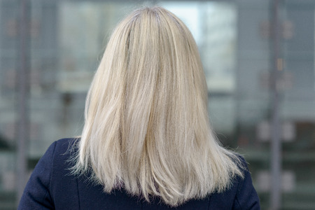 Rear view of a woman with shoulder length blond hair standing in an urban street looking awayの写真素材