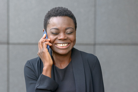 Cheerful smiling African woman chatting on a mobile phone grinning broadly with delight as she...