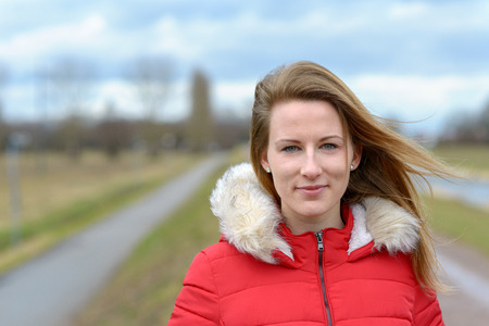 Pretty healthy young woman with long blond hair blowing in the breeze standing in a fur trimmed...
