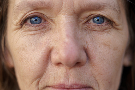 Cropped face of a blue-eyed middle-aged woman with wrinkled skin looking into the lens in a concept of ageingの写真素材