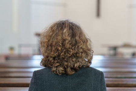 Back view of a Devout religious middle-aged woman praying in a church kneeling alone in a pewの写真素材