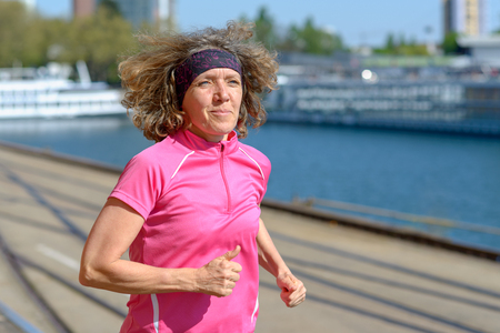 Woman jogging alongside an urban canal or river enjoying her early morning run and daily workout in a health and fitness conceptの写真素材