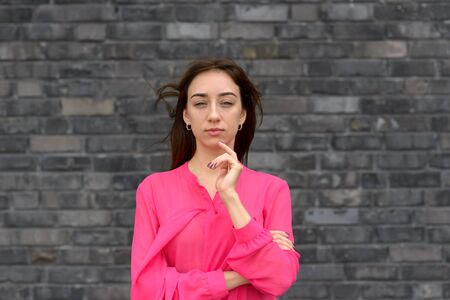 Thoughtful woman standing staring at the camera with her hand to her chin and a contemplative...