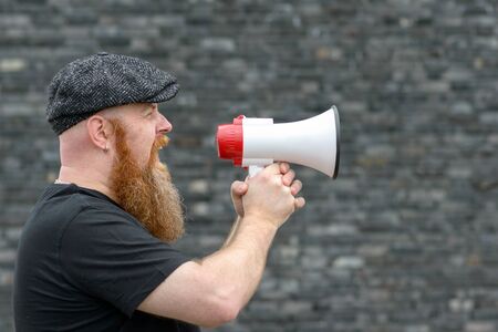 Close up of a Big man yelling into a megaphone at a rally or strike in a communication conceptの写真素材