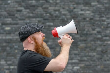Close up of a Man yelling into a megaphone at a rally, strike, demonstration or public speaking at an eventの写真素材