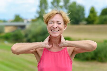 Happy sporty woman stretching with hands to her neck, closed eyes and a beaming smile of appreciation outdoors in a rural landscapeの写真素材