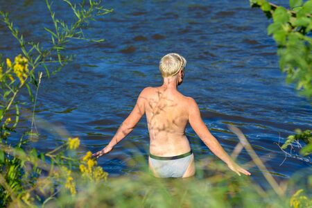 Back view of an attractive blond nude woman going into the lakeの写真素材