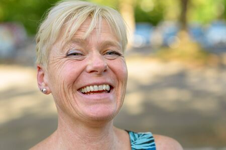 Portrait of an attractive older blond laughing woman outdoors in a park looking to the cameraの写真素材