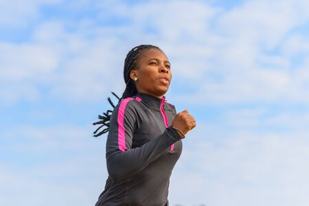 Portrait of an athletic young African woman out for her daily jog passing the camera in a low angle viewの写真素材