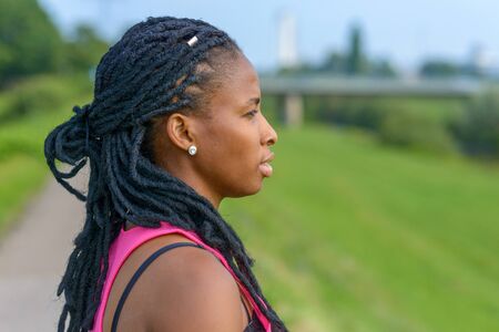 Profile of a thoughtful young African woman wearing hair extensions in braids staring out over lush...