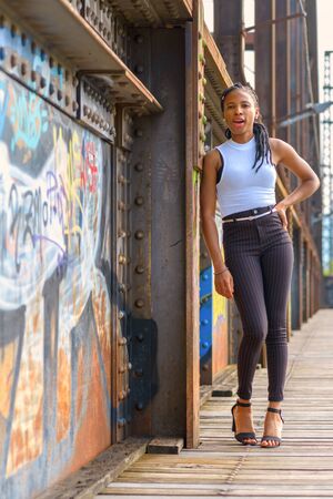 Relaxed stylish sexy young African woman leaning on an old bridge covered in colorful graffiti smiling at the cameraの写真素材