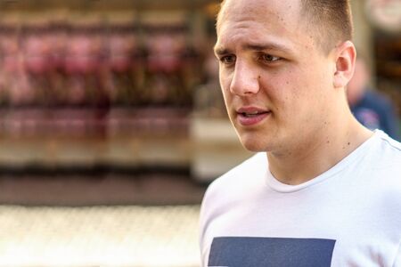 Thoughtful young man in casual T-shirt walking in an urban street with a pensive  look